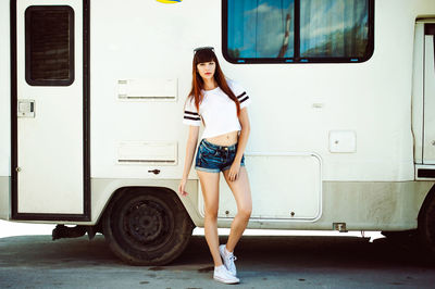 Full length of fashionable young woman standing against vehicle