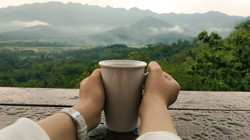Midsection of man with drink against mountains