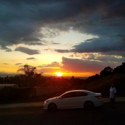 Cars on road amidst field against sky during sunset