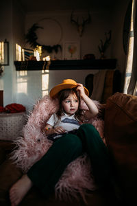 Girl looking out window with yellow hat in home