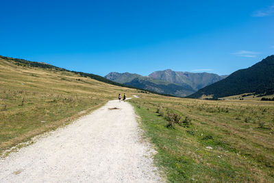 People walking on road by mountain against blue sky