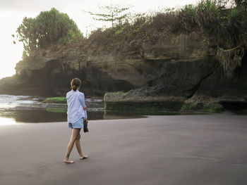 Young woman walking on a rocky beach, looking barefoot