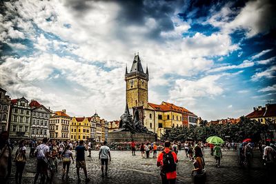 Group of people in front of buildings against cloudy sky