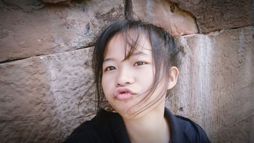 Close-up portrait of girl puckering against stone wall
