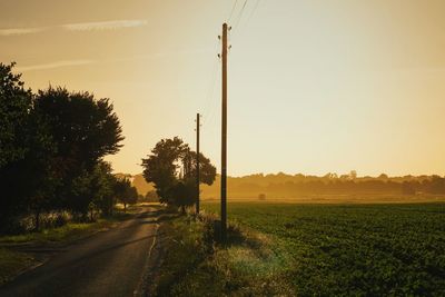 Road amidst field against sky during sunset