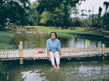 Portrait of smiling woman sitting by lake against trees