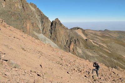 Hiker waking on rocky mountain against sky