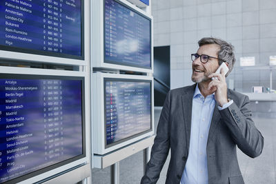 Businessman with cell phone at timetable at the airport