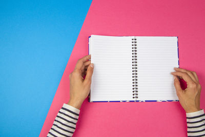 Cropped hands of woman holding notebook over colored background