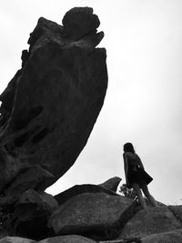 Low angle view of woman standing on rock formation against sky