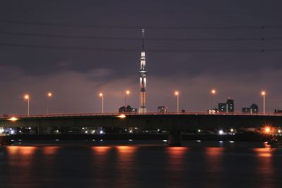 Illuminated bridge over river against sky at night