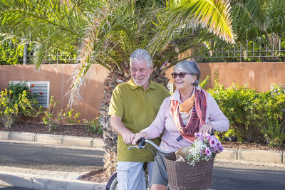 Smiling senior couple riding bicycle while standing outdoors