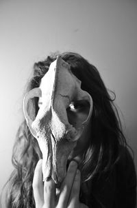 Close-up portrait of woman holding animal skull on face against wall