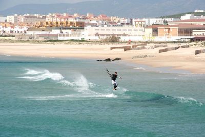 Man windsurfing in sea against cityscape