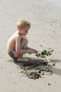 Side view full length of shirtless boy playing with shovel at beach