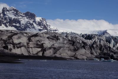 Scenic view of sea by mountain against sky