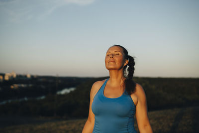 Female athlete with eyes closed against sky during sunset