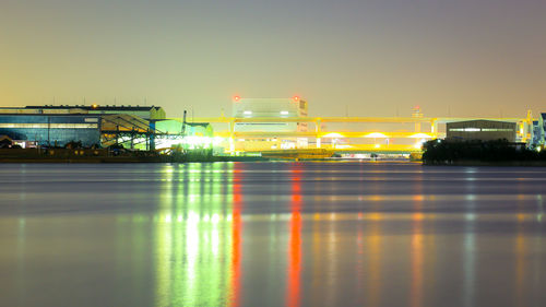 Illuminated buildings by river against sky at night