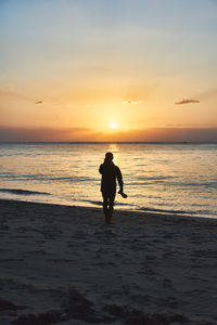 Silhouette man walking on sand at beach against sky during sunset