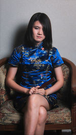 Female model wearing traditional clothing while sitting on chair against wall