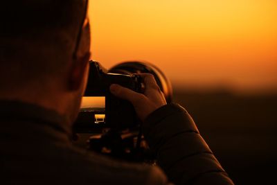 Close-up of man photographing against sky during sunset