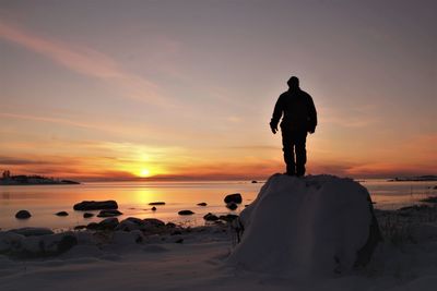 Rear view of man standing on beach against sky during sunset