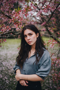 Portrait of beautiful young woman standing by flowering plants