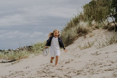 Child girl in jacket laughing and running with clock at the beach