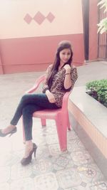 Portrait of beautiful young woman sitting against wall