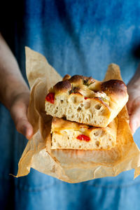 Crop person hands holding piece of fresh tomato focaccia with rosemary