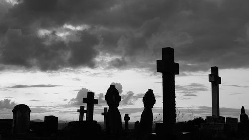 Crosses and tombstones against cloudy sky in cemetery at dusk