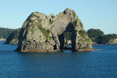 Rock formation in sea against clear blue sky