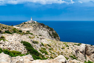 Lighthouse on cliff by sea against sky