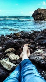 Low section of man relaxing on rock at beach