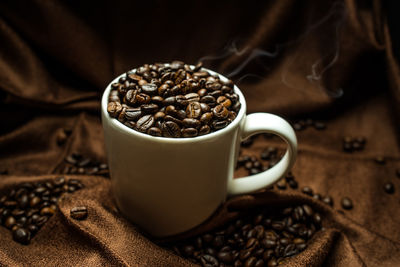 Close-up of roasted coffee beans with cup on fabric