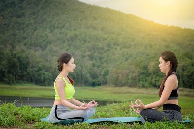 Side view of female friends doing yoga on field against mountain