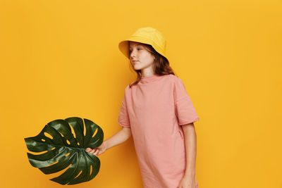 Young woman wearing hat against yellow background