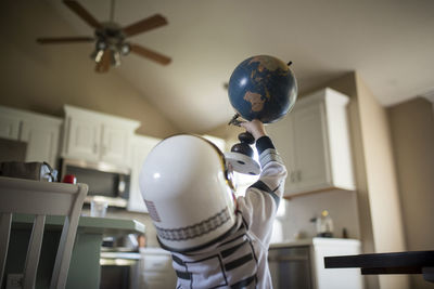 Rear view of boy in astronaut costume holding globe while playing at home