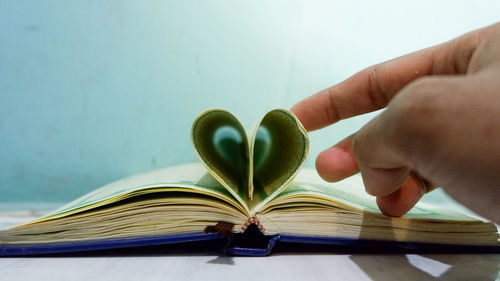Cropped hand of person making heart shape with papers on book