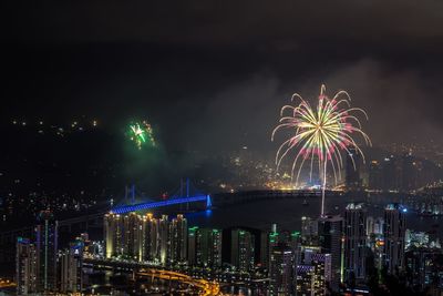 Firework display in city against sky at night