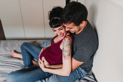 High angle view of pregnant woman sitting with male partner on bed at home