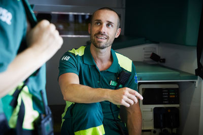 Mid adult paramedic discussing with coworker while sitting in ambulance in parking lot