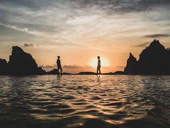 Silhouette people on sea against sky during sunset