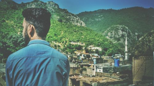 Rear view of man standing against mountains in town