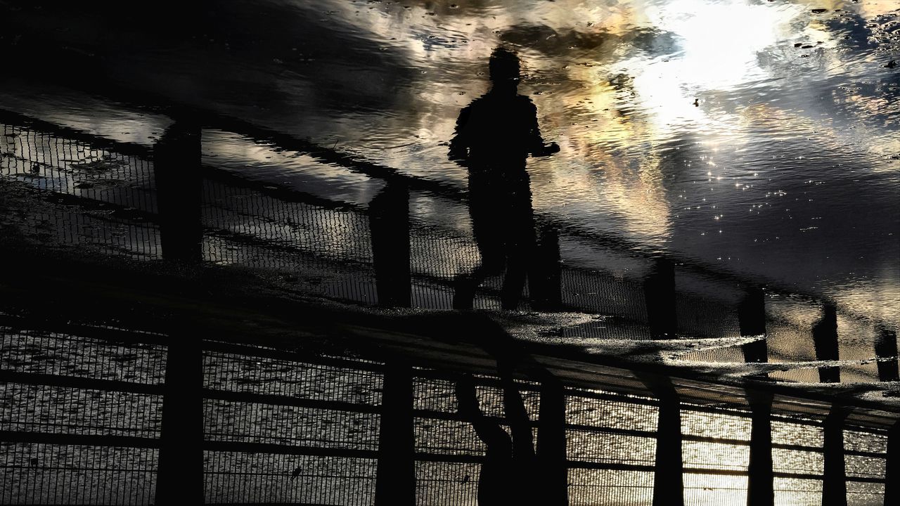 SILHOUETTE MAN STANDING ON RAILING AGAINST WATER