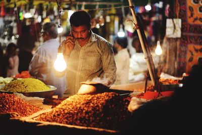 Market vendor answering phone while working at illuminated market stall