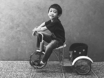 Side view portrait of boy sitting on tricycle by wall