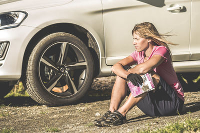 Woman in cycling clothes sitting near car