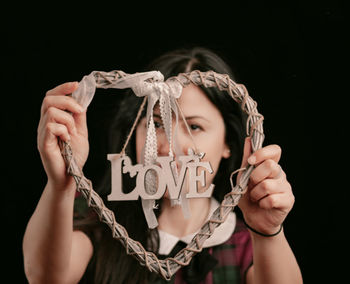 Close-up portrait of a woman holding hands over black background