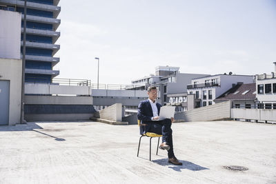 Smiling businessman with laptop sitting on chair